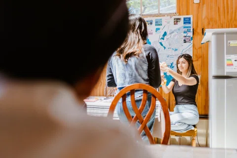 Mujer sentada durante el maquillaje, vista por encima del hombro de otra persona.