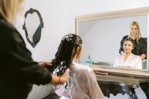 Mujer sentada frente a un espejo mientras otra persona acomoda su cabello.