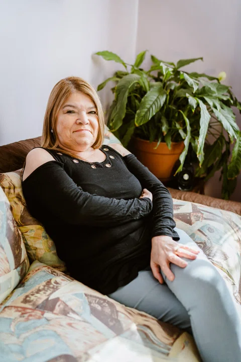 Mujer sentada en un sofá junto a plantas de interior.
