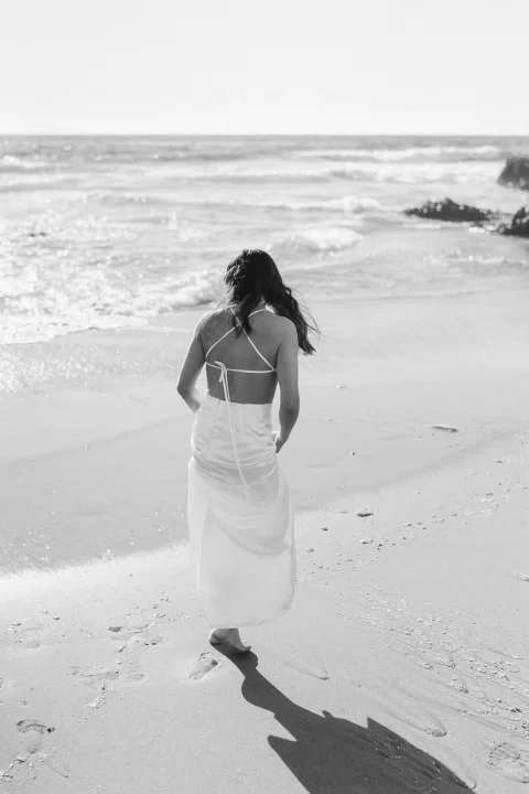 Mujer caminando sola por la playa en una fotografía en blanco y negro.