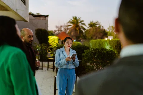 Mujer con traje celeste habla frente a varias personas en un jardín.