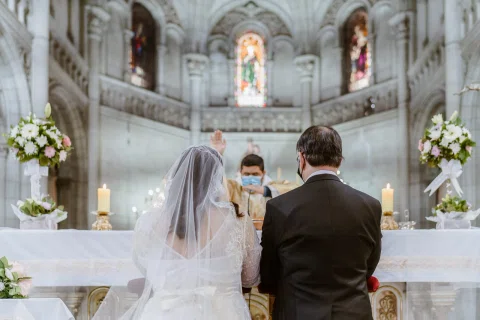 Mujer con velo y hombre con traje oscuro permanecen arrodillados frente al altar.