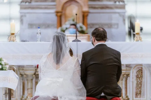 Mujer con velo y hombre con traje oscuro aparecen de espaldas frente al altar de una iglesia.