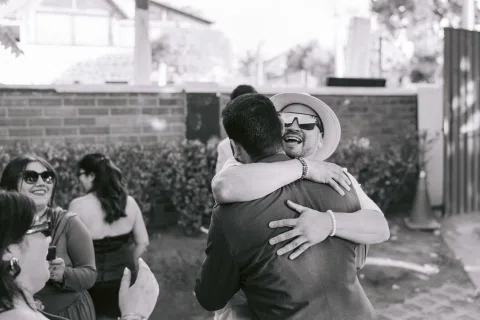 Mujer con vestido blanco abraza a un hombre de espaldas, en una fotografía en blanco y negro.