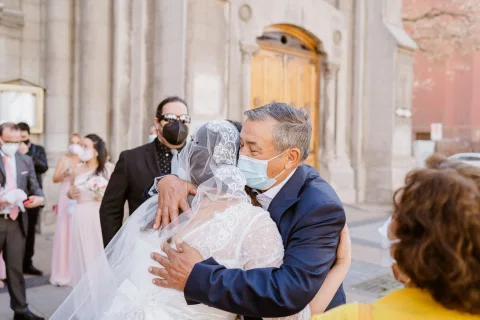 Mujer con vestido blanco abraza a un hombre con traje azul en el exterior de una iglesia.