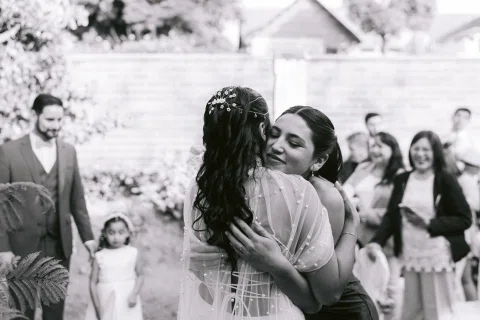 Mujer con vestido blanco abraza a otra mujer, en una fotografía en blanco y negro.