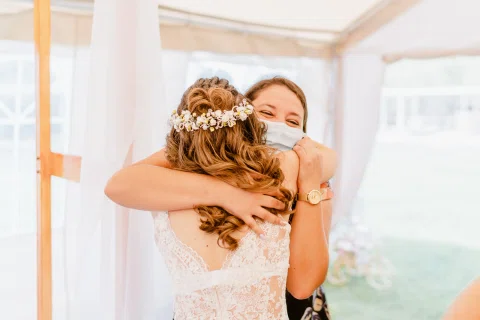 Mujer con vestido blanco abrazando a otra mujer bajo la carpa.