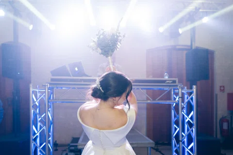 Mujer con vestido blanco aparece de espaldas frente a luces intensas y la cabina de música.