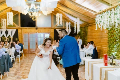 Mujer con vestido blanco baila tomada de la mano de un hombre con chaqueta azul entre las mesas.