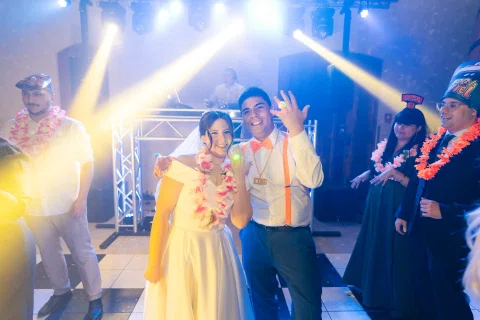 Mujer con vestido blanco baila junto a un hombre con camisa blanca y tirantes bajo luces de escenario.
