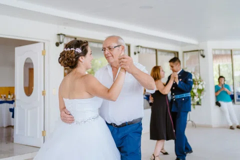 Mujer con vestido blanco bailando con un hombre mayor en un salón.