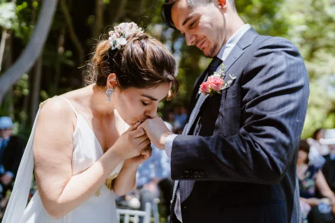 Mujer con vestido blanco besa la mano de un hombre con traje oscuro.