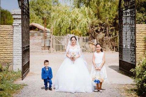 Mujer con vestido blanco caminando por el jardín junto a dos niños.