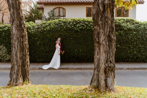 Mujer con vestido blanco posando a distancia entre dos troncos de árbol.