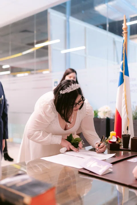 Mujer con vestido blanco escribe sobre un documento en una mesa.