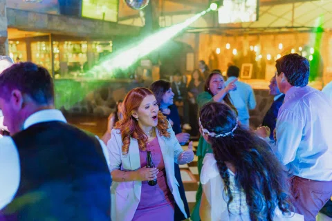 Mujer con vestido blanco, vista de espaldas, está frente a una mujer pelirroja que sostiene una botella en la pista.