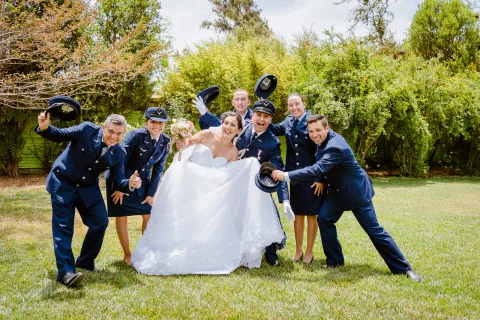 Mujer con vestido blanco posa sobre el césped junto a un grupo de personas con uniforme azul.