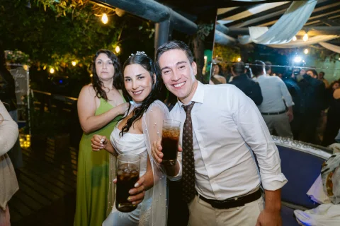 Mujer con vestido blanco y hombre con camisa blanca posan juntos sosteniendo vasos.