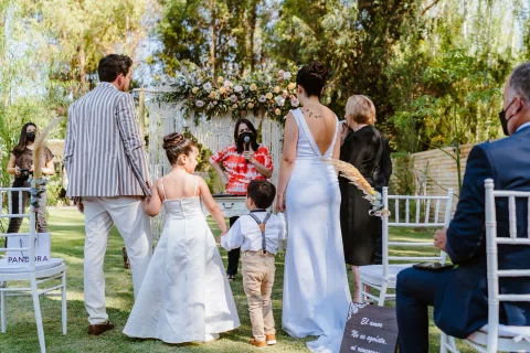 Mujer con vestido blanco y hombre con chaqueta a rayas vistos de espaldas junto a dos niños.