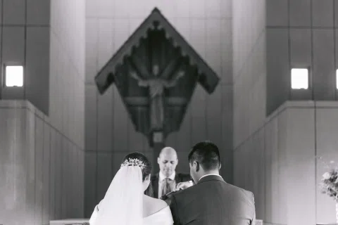 Mujer con vestido blanco y hombre con traje azul aparecen de espaldas junto a un hombre mayor, en blanco y negro.