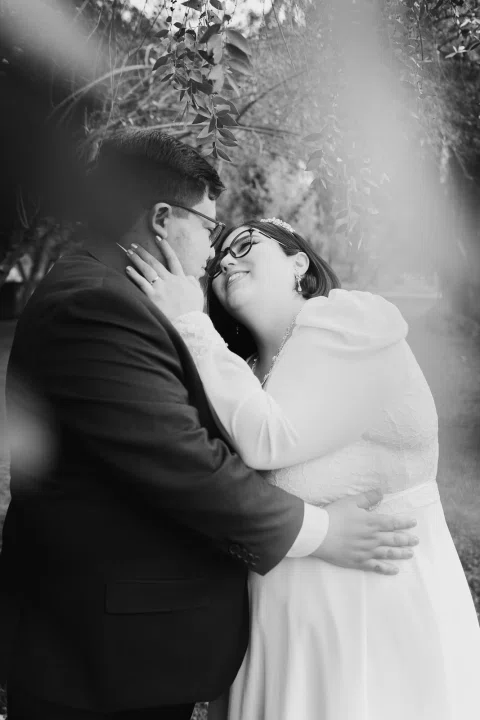 Mujer con vestido blanco y hombre con traje oscuro se besan en un retrato cercano en blanco y negro.