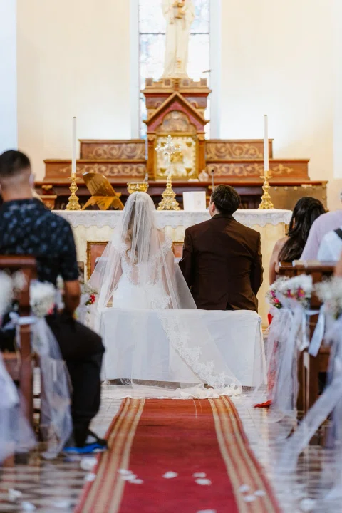 Mujer con vestido blanco y hombre con traje oscuro vistos de espaldas frente al altar de una iglesia.