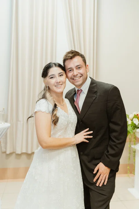 Mujer con vestido blanco posa junto a un hombre con traje oscuro y corbata roja.