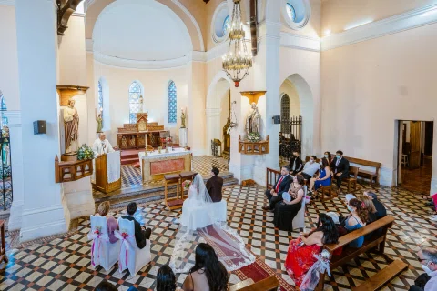 Mujer con vestido blanco y hombre con traje oscuro sentados juntos cerca del altar.