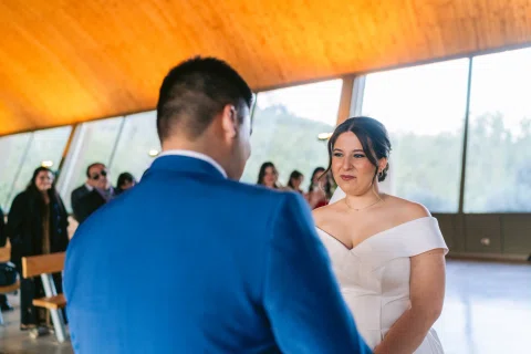 Mujer con vestido blanco mira a un hombre con traje azul frente al altar.