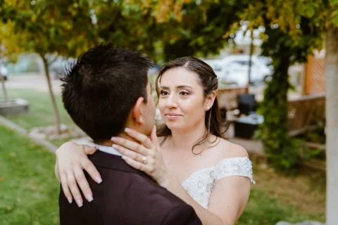 Mujer con vestido blanco mira a un hombre con traje oscuro mientras lo abraza en un retrato cercano.