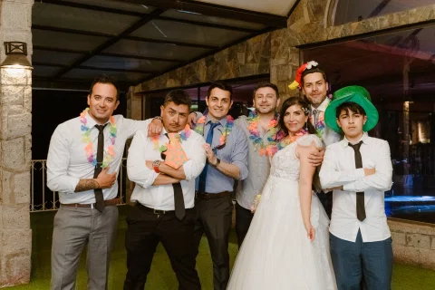 Mujer con vestido blanco posa con un grupo de hombres que llevan collares y accesorios de fiesta.