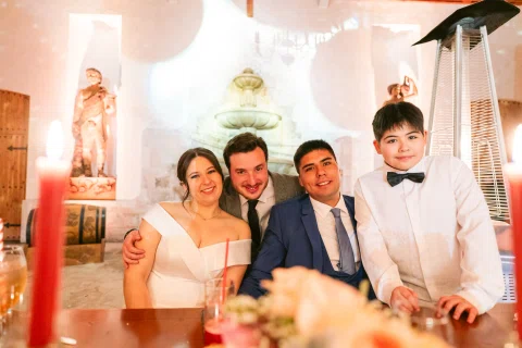 Mujer con vestido blanco posa sentada junto a tres hombres detrás de una mesa decorada.
