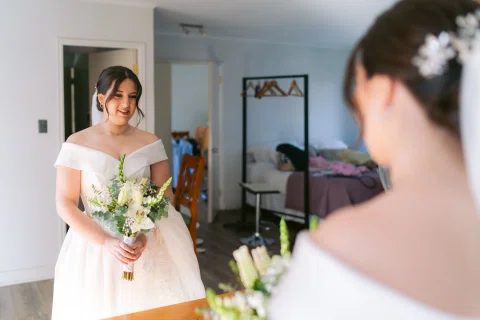 Mujer con vestido blanco y ramo se observa frente a un espejo.