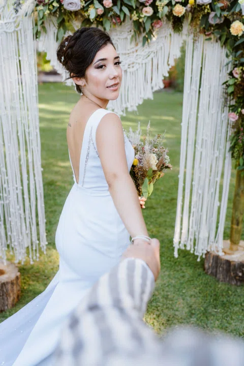 Mujer con vestido blanco posa sola de perfil con la espalda del vestido visible.
