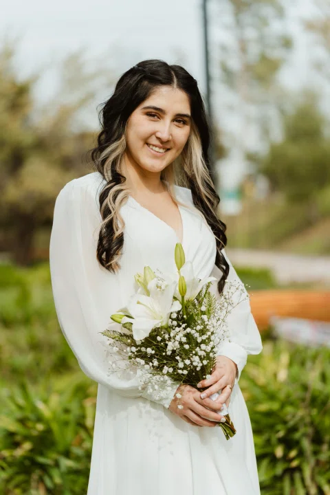 Retrato de una mujer con vestido blanco sosteniendo un ramo en un parque.