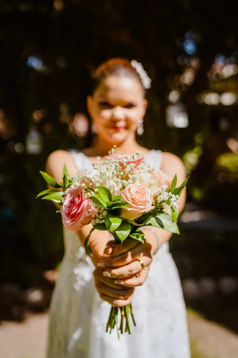 Mujer con vestido blanco posa sola con un ramo de flores coloridas frente a un fondo oscuro.