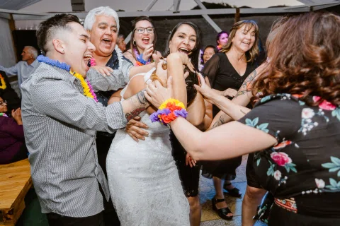 Mujer con vestido blanco aparece rodeada por varias personas en un momento animado, con brazos y manos alrededor de ella.