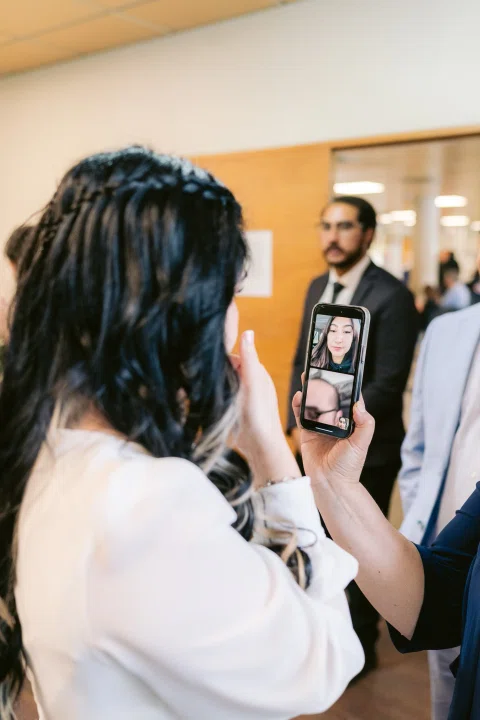 Mujer con vestido blanco sostiene un celular cuya pantalla muestra el rostro de otra mujer.
