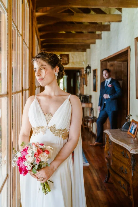 Mujer con vestido blanco sostiene un ramo dentro de un interior de madera.