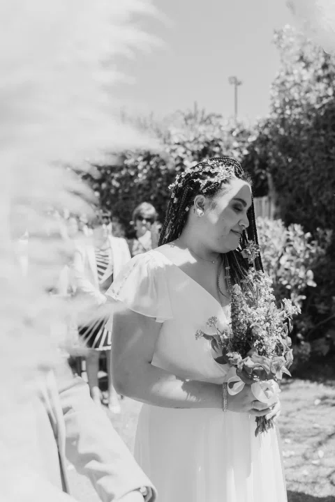 Mujer con vestido blanco sostiene un ramo y mira hacia un costado, en blanco y negro.