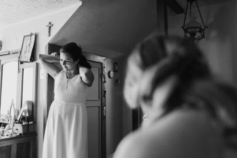Mujer con vestido blanco toca su cabello junto a una ventana, en blanco y negro.