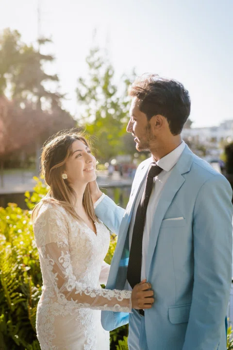 Mujer con vestido blanco toca la solapa de un hombre con traje celeste en un retrato a contraluz.