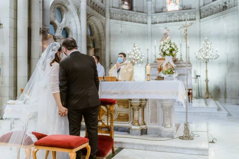 Mujer con vestido blanco y hombre con traje oscuro permanecen juntos frente al altar de una iglesia.