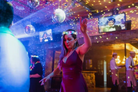 Mujer con vestido burdeo y una corona luminosa baila con un brazo levantado bajo luces de colores.