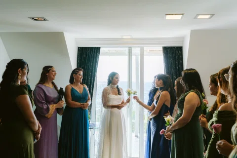 Varias mujeres rodean a una mujer con vestido blanco dentro de una habitación.