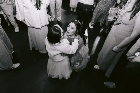 Niña abraza a una mujer agachada entre varias personas, en una fotografía en blanco y negro.
