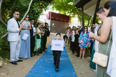Niño con traje negro camina por una alfombra azul sosteniendo un cartel.