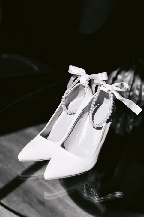 Par de zapatos blancos con lazos fotografiado en blanco y negro sobre una superficie oscura.