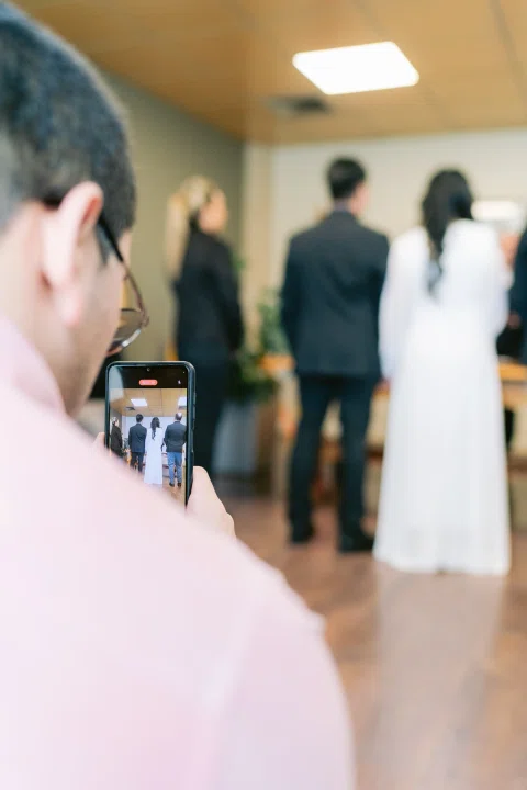 Persona sostiene un celular en primer plano mientras un grupo aparece desenfocado al fondo.
