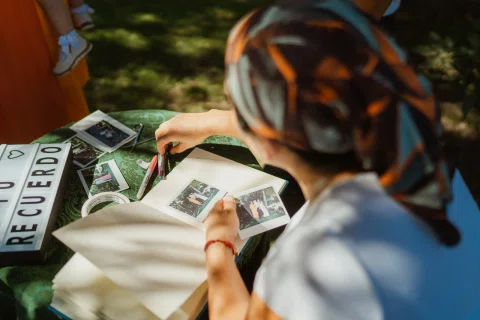 Persona coloca fotografías instantáneas en un álbum abierto sobre una mesa exterior.